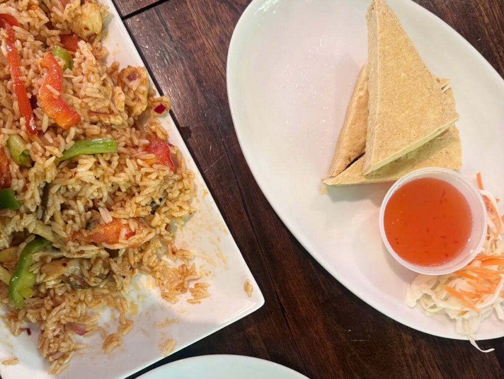 A plate of fried rice with vegetables, including red peppers and green bell peppers, next to a plate with two folded tortillas, a small cup of dipping sauce, and a side of coleslaw. The Baht Gatlinburg is the dining setting.