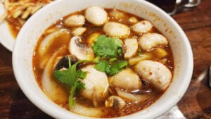 Bowl of Tom Yum soup at The Baht featuring mushrooms, fish balls, herbs, and spicy Thai broth